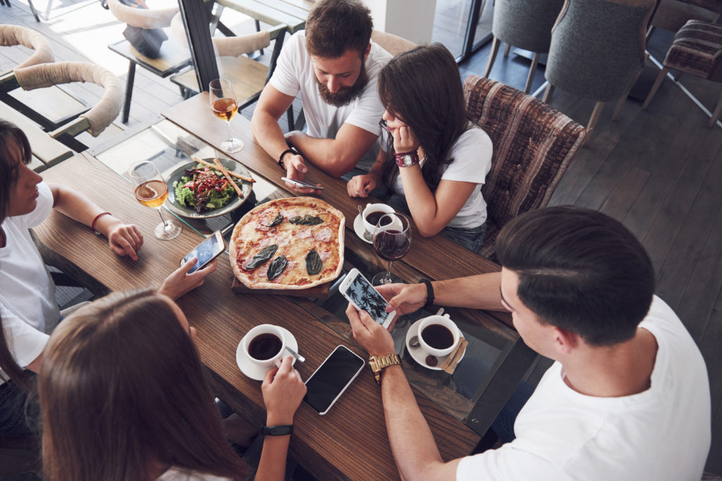 Tasty pizza on the table, with a group of young smiling people resting in the pub.